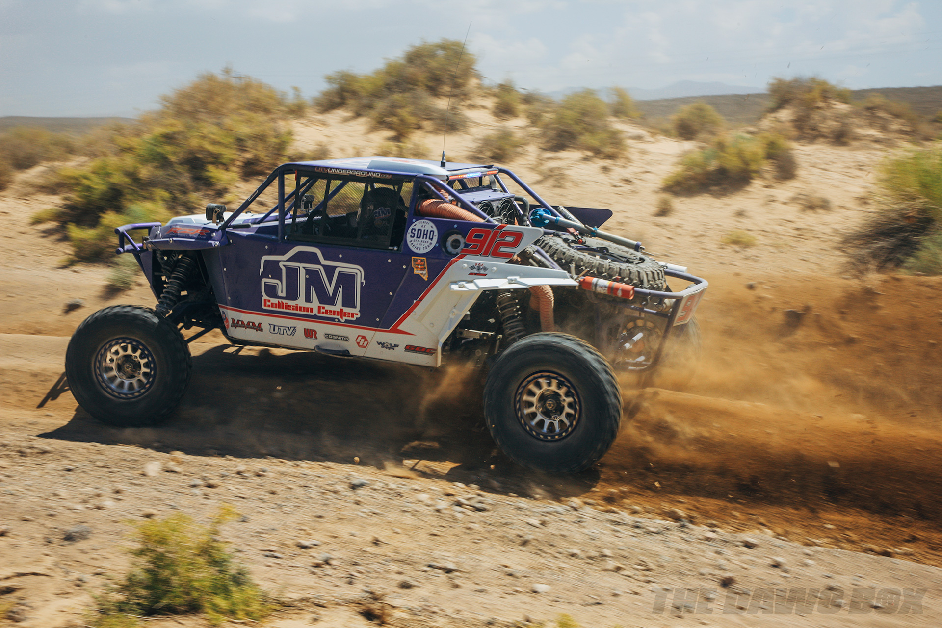 Blue JM Collision Center Rock racer speeding over a desert dirt road