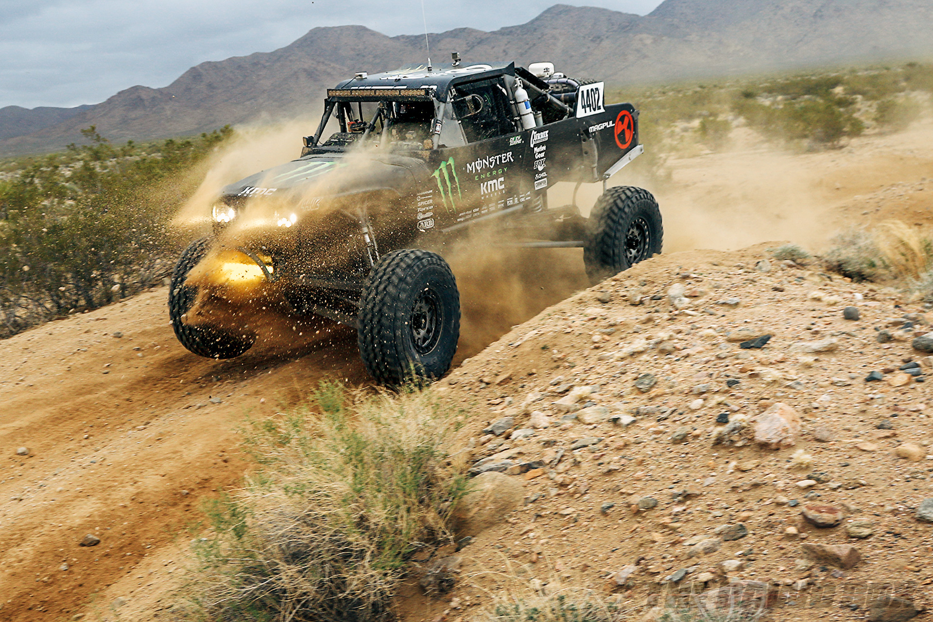 Black, Monster Energy sponsored rock racer speeding over a desert road