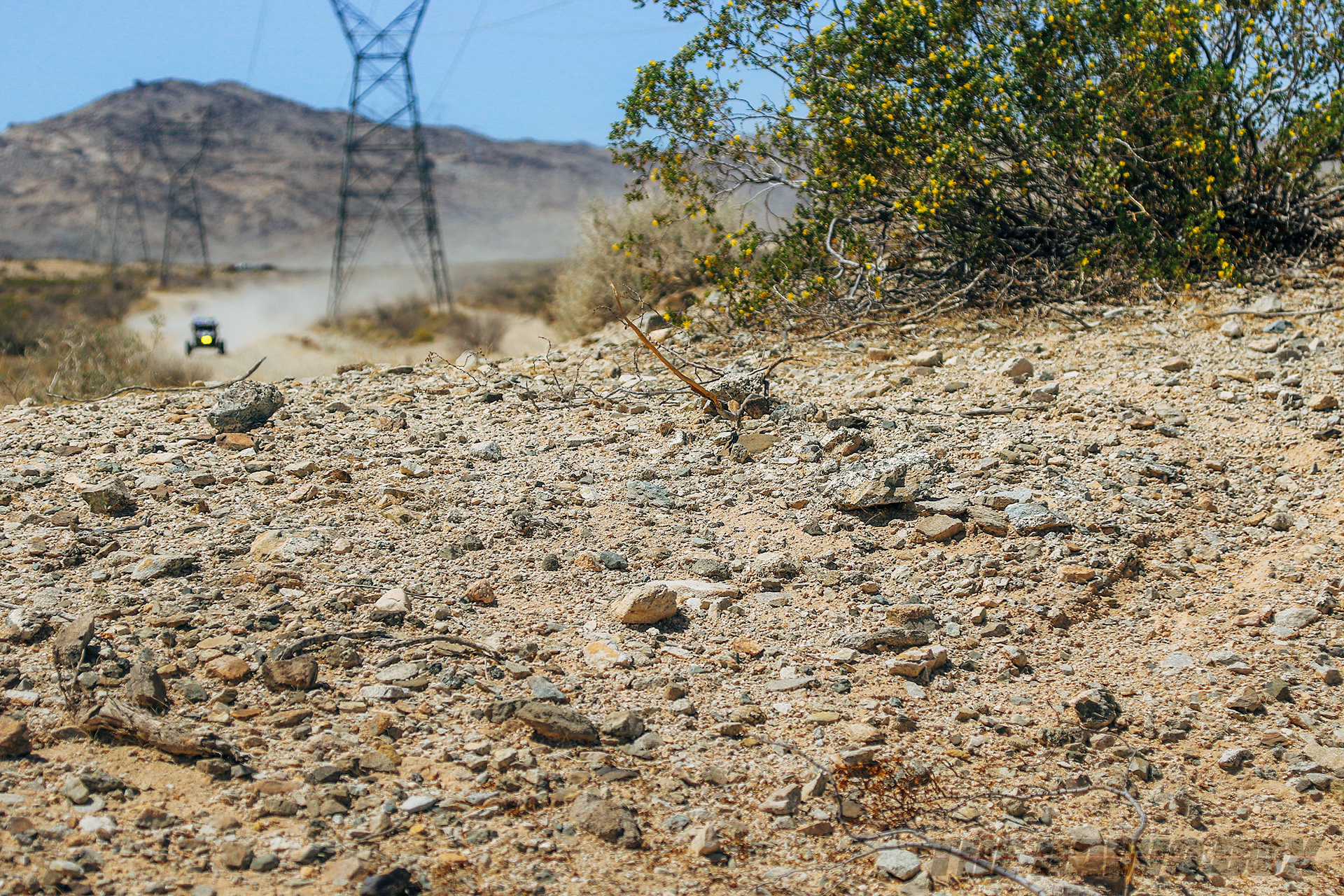 Close up of a dirt road while a rock racer speeds towards the camera in the distance