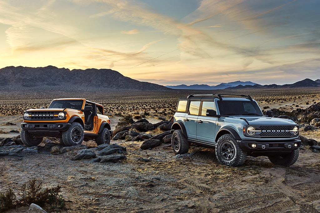 Pre-production versions of the 2021 Bronco, shown here, include Bronco two-door in Cyber Orange Metallic Tri-Coat and Bronco four-door in Cactus Gray in a mountainous desert during sunset
