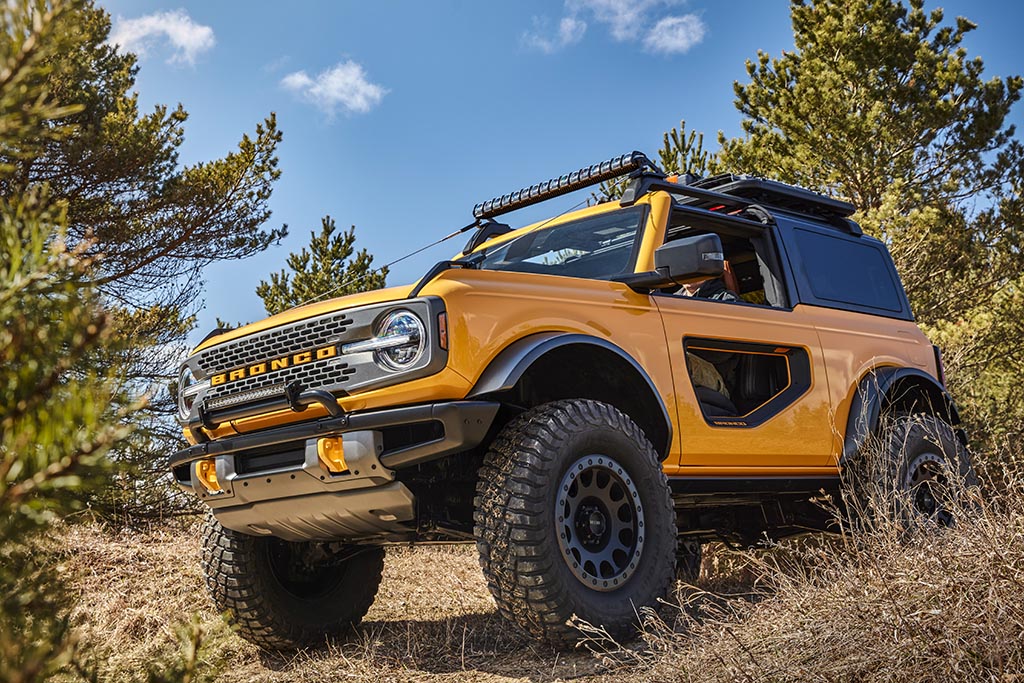 Yellow 2021 Ford Bronco with modular windowed doors trekking through a forest on a sunny day