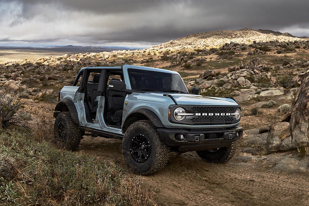 Pre-production 2021 Bronco four-door Badlands series with available Sasquatch™ off-road package in Cactus Gray with the doors, top and rear quarter windows removed in a rocky desert during a cloudy day