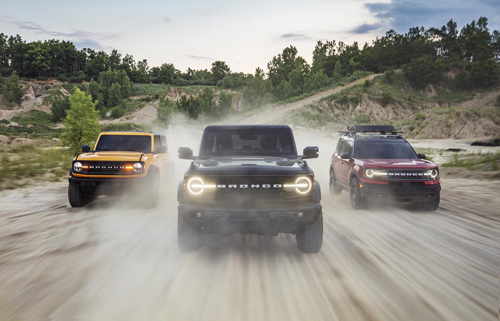 Pre-production versions of the all-new 2021 Bronco family of all-4x4 rugged SUVs, shown here, include (left) Bronco two-door in Cyber Orange Metallic Tri-Coat, Bronco four-door in Shadow Black and Bronco Sport in Rapid Red Metallic Tinted Clearcoat, all speeding through a forest dirt road.