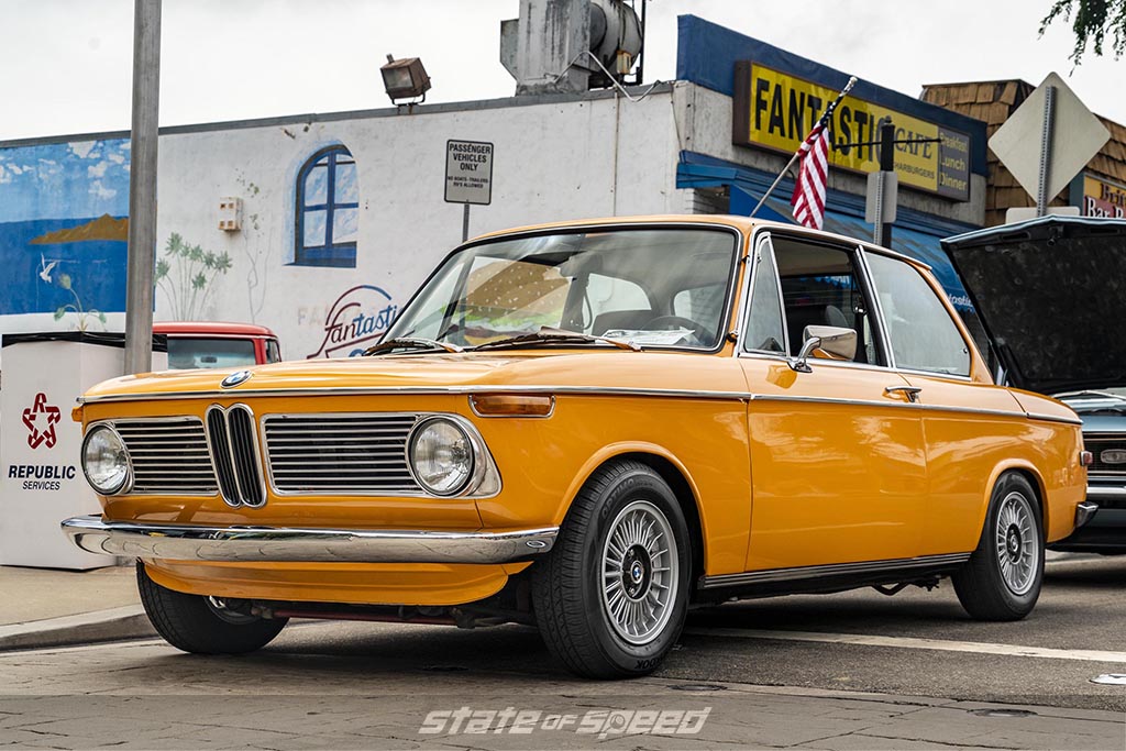 Orange 1960's BMW 2002 in front of a store at a car meet during an overcast day