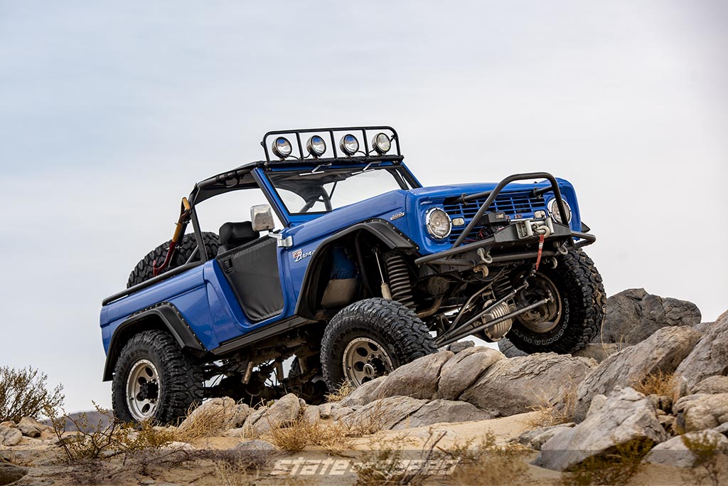 custom Blue first generation 1966 Ford Bronco crawling over some rocks in a desert